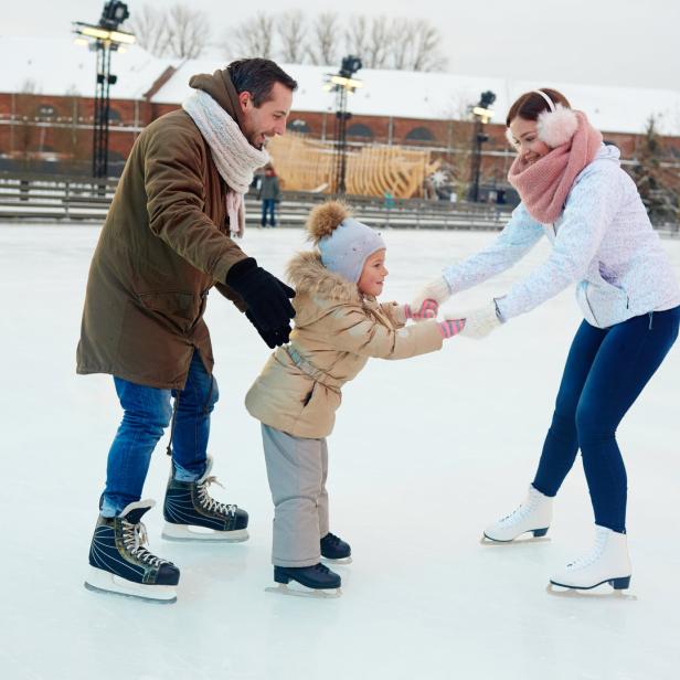 Eine Familie hilft einem kleinen Kind beim Eislaufen auf einer Eisbahn.