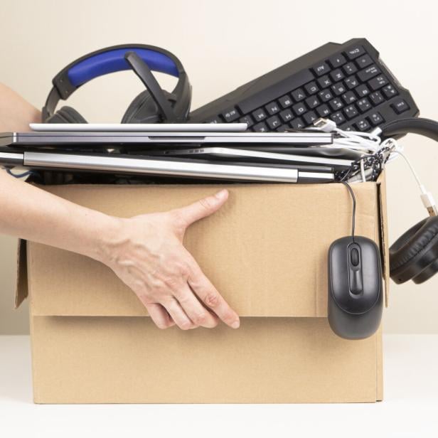 Eine Person hält einen Karton voller Laptops, Kopfhörer, einer Maus und einer Tastatur.