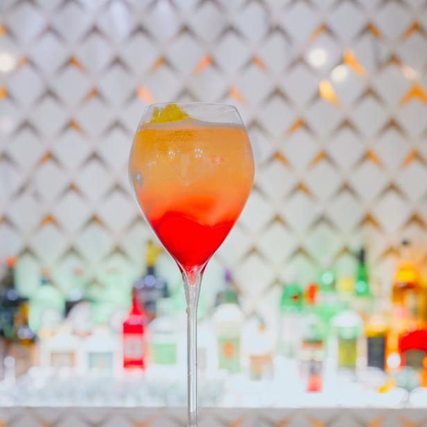 Ein Cocktail mit rotem und orangem Farbverlauf in einem Weinglas.