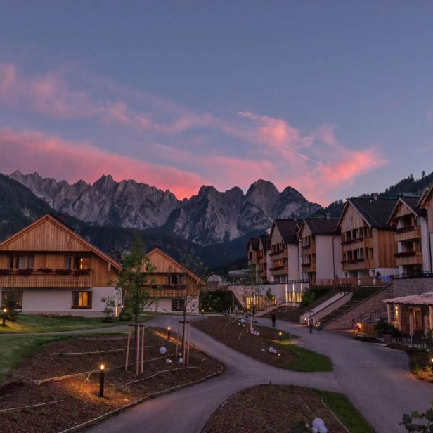 Häuser im alpenländischen Stil vor einer Bergkulisse bei Sonnenuntergang.