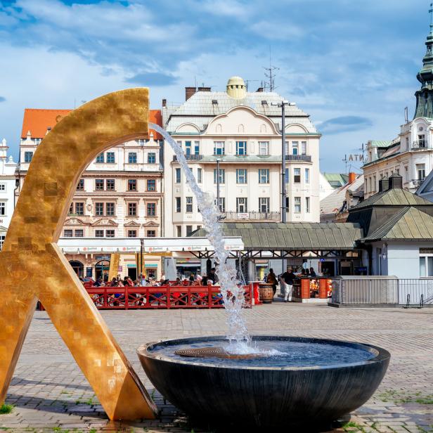 Ein goldener Brunnen auf einem belebten Platz in einer europäischen Stadt.