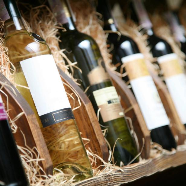 Mehrere Weinflaschen liegen in einem hölzernen Weinregal mit Stroh.