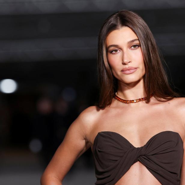 Hailey Bieber trägt ein trägerloses, braunes Oberteil und eine orangefarbene Halskette.