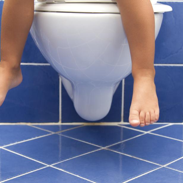 Ein Kind sitzt auf einer Toilette vor blau gefliesten Wänden.