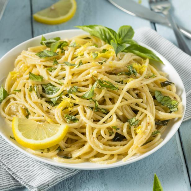 Ein Teller Spaghetti mit Zitrone und Basilikum auf einem hellblauen Tisch.