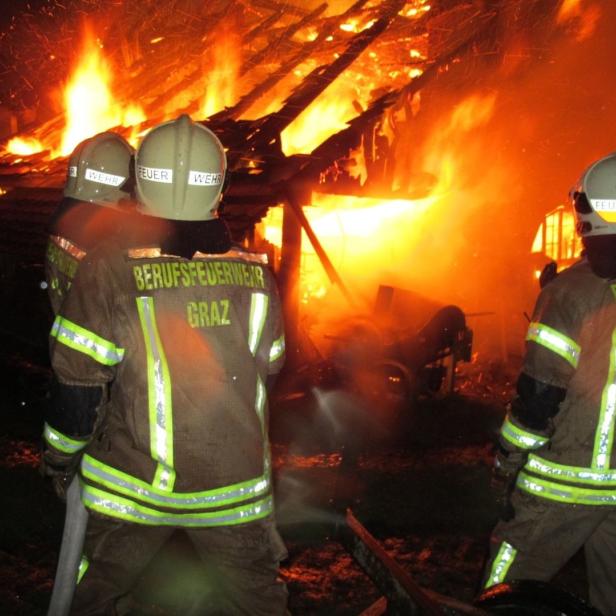Feuerwehrleute der Berufsfeuerwehr Graz stehen vor einem brennenden Gebäude.