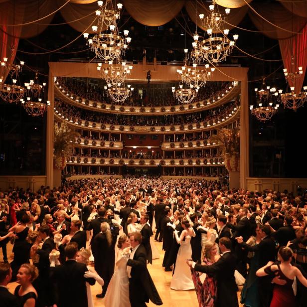 Ein großer Ballsaal mit vielen Paaren beim Tanzen unter funkelnden Kronleuchtern.