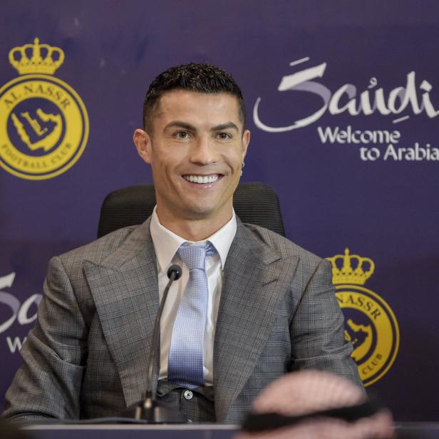 Cristiano Ronaldo lächelt vor einem Hintergrund mit dem Logo von Al-Nassr.