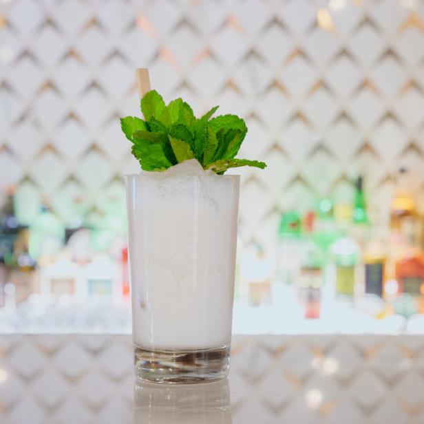 Ein weißer Cocktail mit Minze steht auf einer Bar.