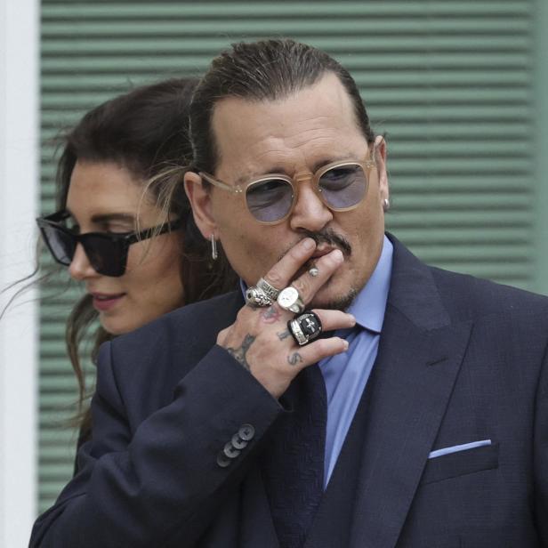 Johnny Depp mit Sonnenbrille und Anzug, eine Hand am Mund, neben einer Frau.