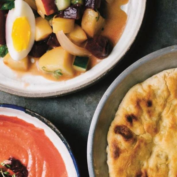Drei Schalen mit Rote Bete-Salat, Tomatensuppe und Fladenbrot stehen auf einem Tisch.