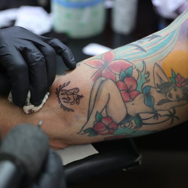 Ein Tätowierer sticht ein neues Tattoo auf den Arm einer Person mit bestehenden Tätowierungen.