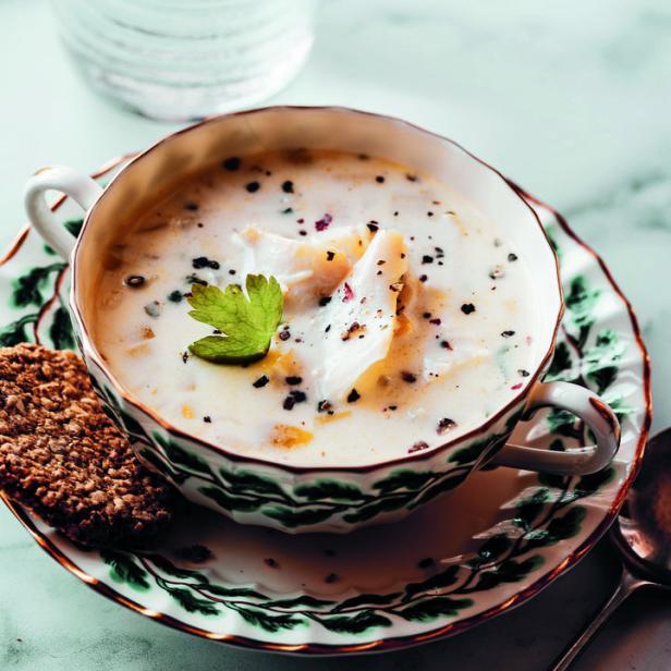 Eine Tasse cremige Suppe mit einem Keks und einem Glas Wasser auf einem Marmortisch.