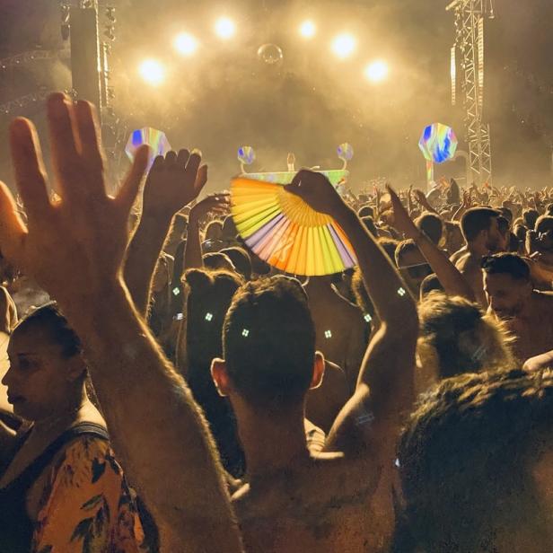 Eine Menschenmenge feiert auf einem Konzert mit Lichteffekten und einer Discokugel.