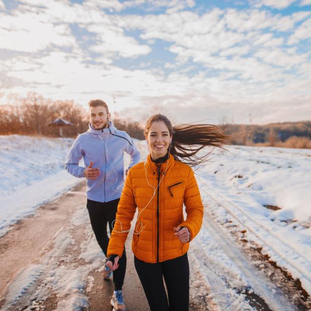 Ein Paar joggt im Winter auf einer schneebedeckten Straße.