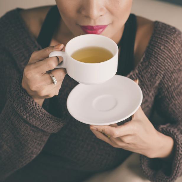Eine Frau mit rotem Lippenstift trinkt Tee aus einer weißen Tasse.