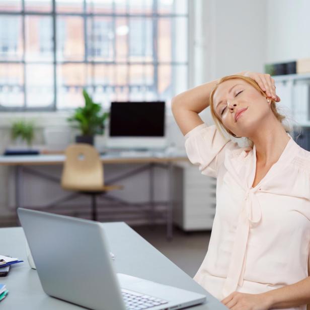 Eine Frau dehnt ihren Nacken am Schreibtisch im Büro.