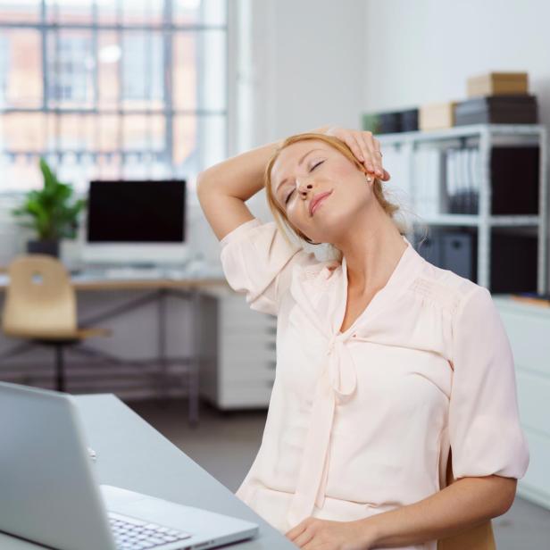 Eine Frau dehnt ihren Nacken am Schreibtisch im Büro.