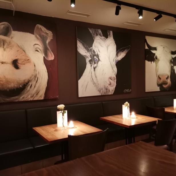 Ein Restaurant mit Gemälden von Schwein, Ziege und Kuh an der Wand.