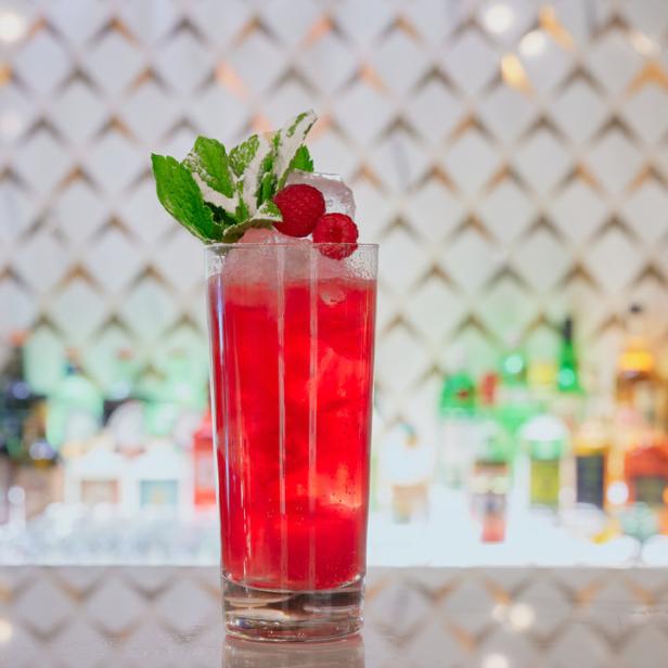 Ein roter Cocktail mit Himbeeren und Minze steht auf einer Bar.