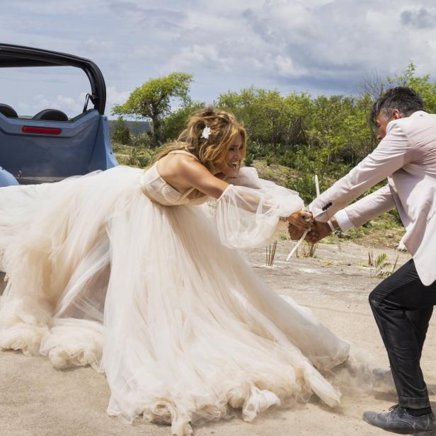 Eine Braut im Hochzeitskleid wird von einem Mann auf einem staubigen Feld zurückgehalten.