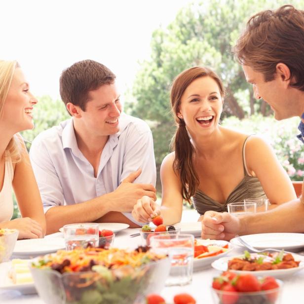 Vier Freunde sitzen lachend bei einem Essen im Freien zusammen.