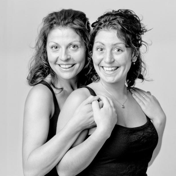 Zwei lächelnde Frauen umarmen sich in einem Schwarzweißfoto.