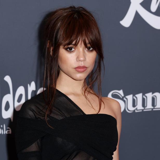 Jenna Ortega posiert vor einer Wand mit Sponsorenlogos.