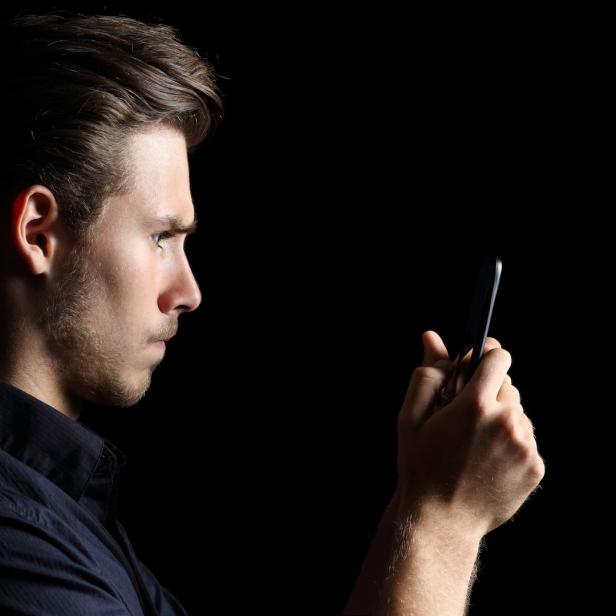Ein Mann im Profil, der auf sein Smartphone schaut.