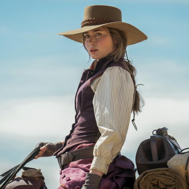 Emily Blunt reitet in Westernkleidung auf einem Pferd vor blauem Himmel.