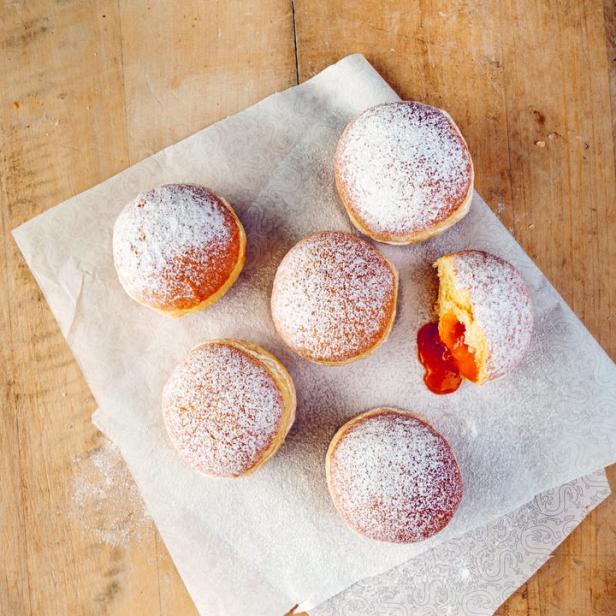 Sechs mit Puderzucker bestäubte Krapfen liegen auf einem Stück Papier.