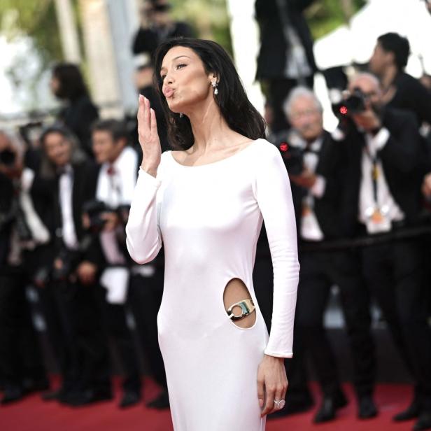 Bella Hadid in einem weißen Kleid auf dem roten Teppich, umringt von Fotografen.