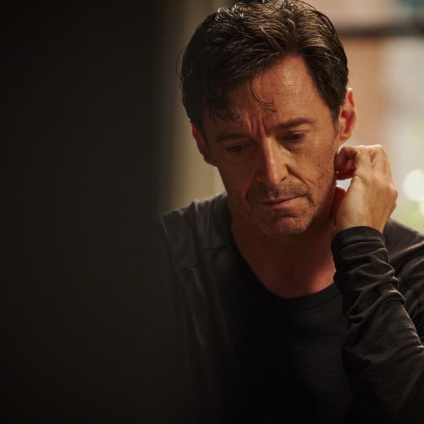 Hugh Jackman wirkt nachdenklich, während er seine Hand an seine Wange hält.