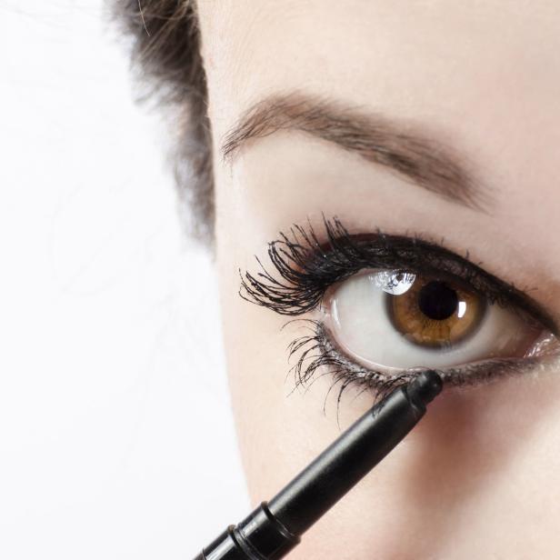 Eine Frau trägt schwarzen Eyeliner auf das untere Augenlid auf.
