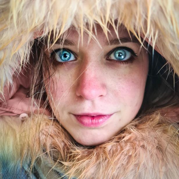 Nahaufnahme einer jungen Frau mit strahlend blauen Augen und einer Kapuze mit Fellrand.