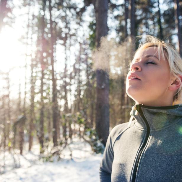 Eine Frau atmet im Winterwald die kalte Luft ein.
