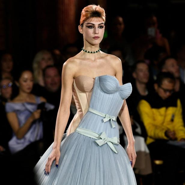 Ein Model präsentiert ein trägerloses Kleid mit hellblauem Tüllrock auf dem Laufsteg.