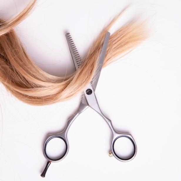 Eine blonde Haarsträhne wird mit einer Effilierschere geschnitten.