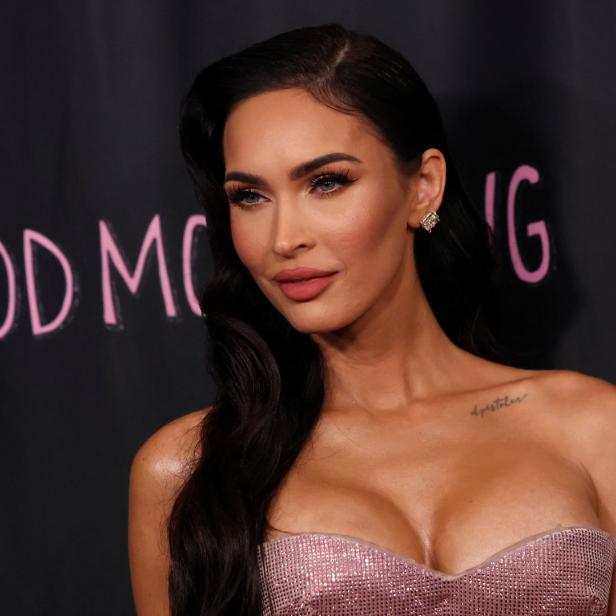 Megan Fox posiert vor einer Wand mit der Aufschrift „Good Morning“.