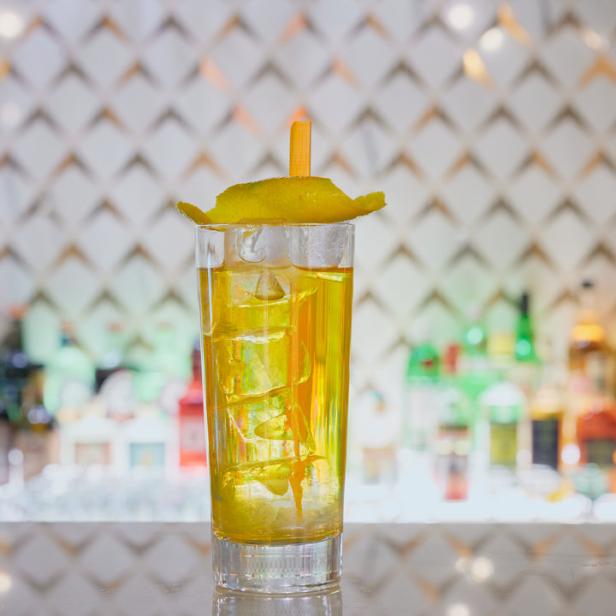 Ein Longdrink mit Eiswürfeln und einer Zitronenzeste an einer Bar.