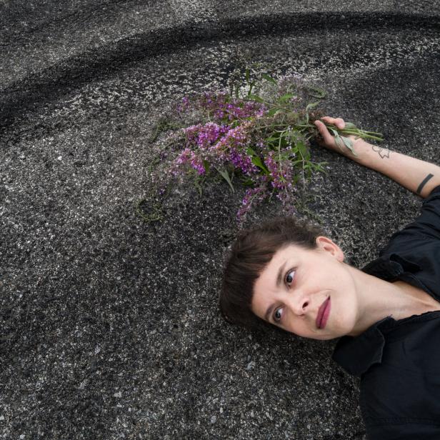 Eine Frau liegt auf dem Asphalt und hält einen Strauß lila Blumen.