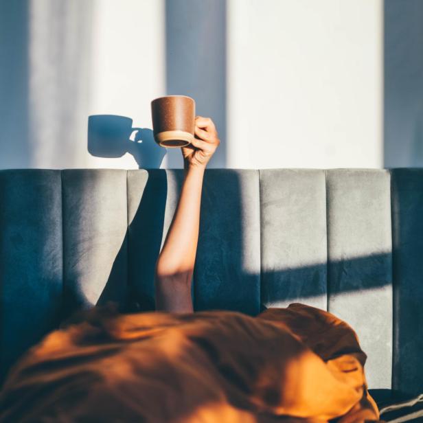 Eine Person liegt im Bett und hält eine Tasse in der Hand.