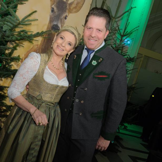 Ein Mann und eine Frau in Tracht posieren vor einem Weihnachtsbaum und einem Hirschbild.
