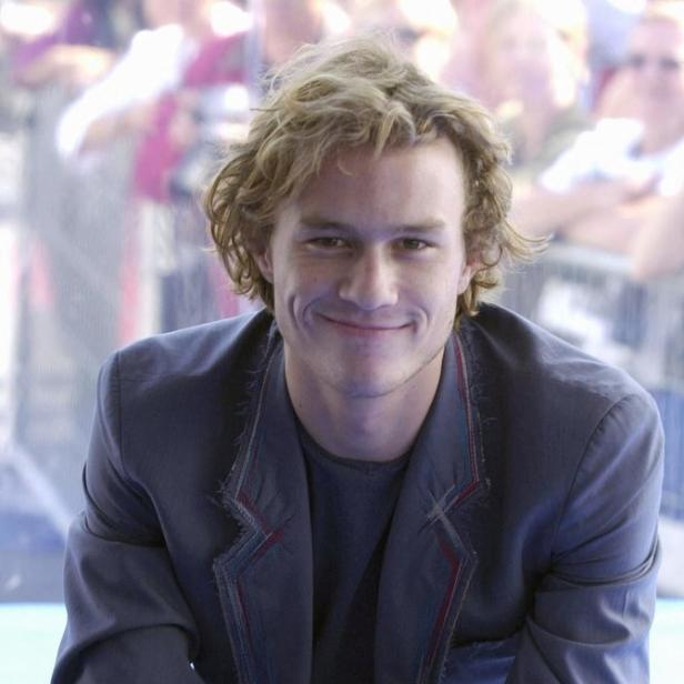 Heath Ledger sitzt und lächelt in einem blauen Anzug.
