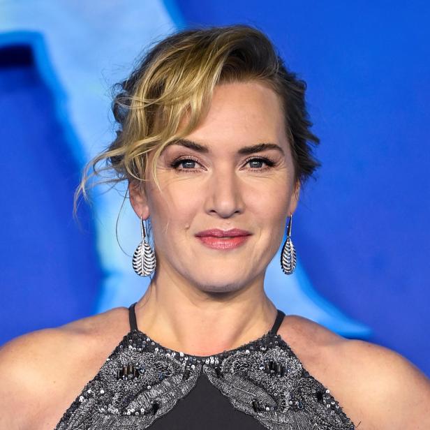 Ein Porträt von Kate Winslet mit silbernen Ohrringen vor einem blauen Hintergrund.