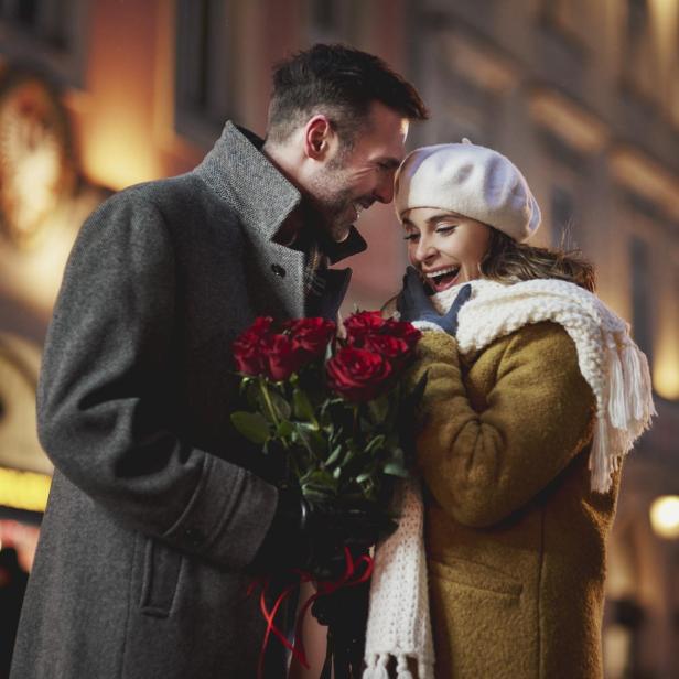 Ein Mann schenkt einer überraschten Frau einen Strauß roter Rosen zum Valentinstag.
