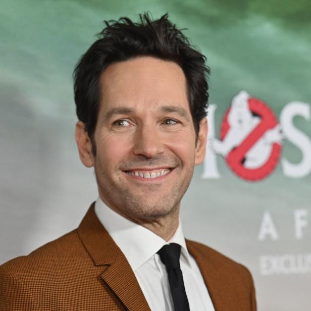 Paul Rudd lächelt vor einem „Ghostbusters: Afterlife“-Poster.
