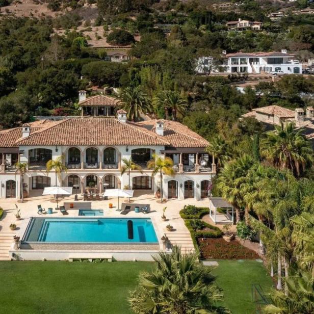 Ein großes, weißes Haus mit Pool liegt inmitten einer grünen Landschaft.