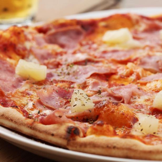 Eine Pizza Hawaii mit Schinken und Ananas auf einem Teller.
