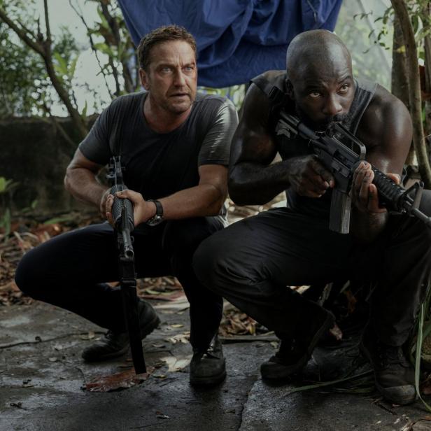 Gerard Butler und Idris Elba zielen mit Gewehren in einer Dschungelartigen Umgebung.